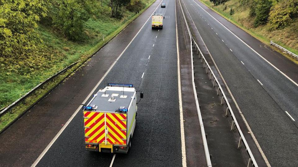 ATO team travelling along the motorway, one vehicle is clearly in shot with yellow and red stripes on its back panel, the roof is grey and the rest of the vehicle appears to be white.