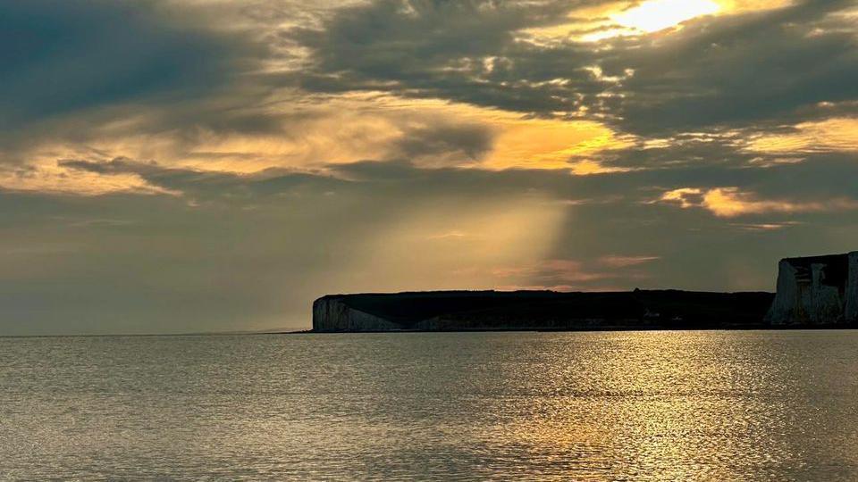 The sea with cliffs in the horizon with sun rays breaking through the clouds 