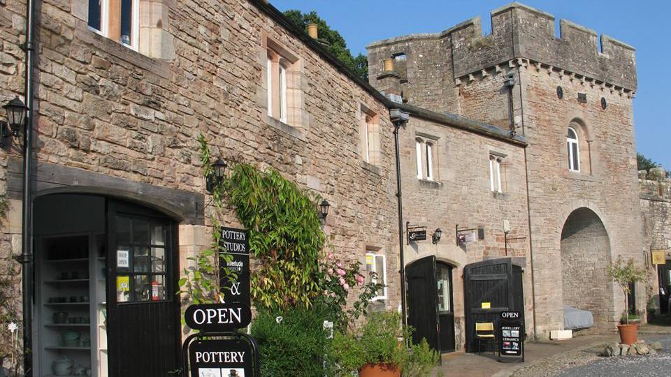 A large, stone building with a turret. There are various entrances, the closest one is a pottery studio. 