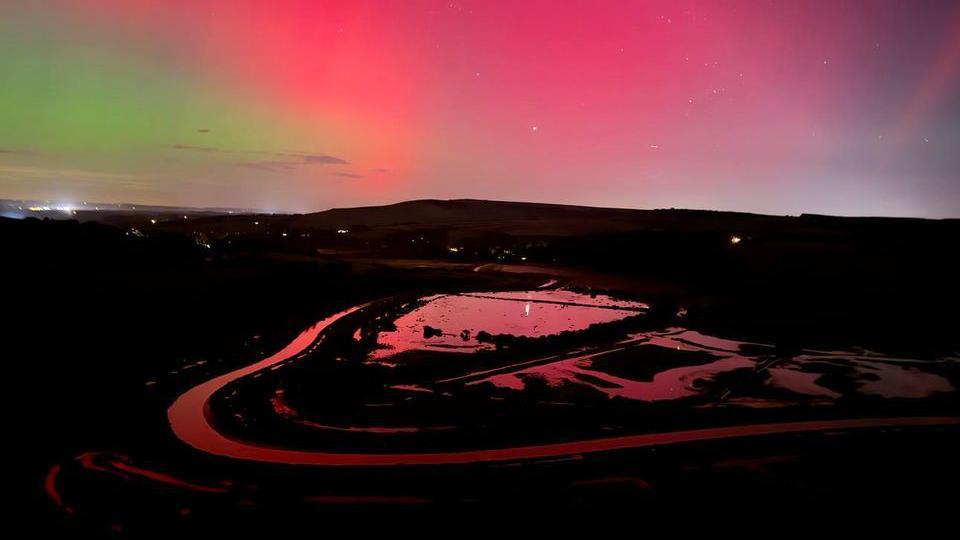 A river is lit up red under the Northern Lights