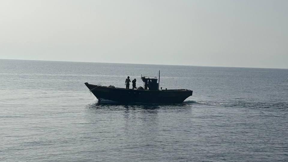 A wooden boat in the middle of the sea. Two people are seen standing on the boat