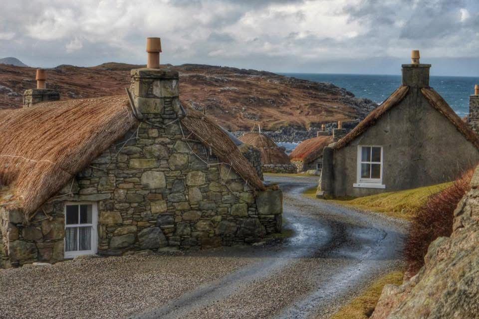 Some stone built houses sut into the ground. They have thatched roofs. A road twists through them and is curiously at a height that is half way up the houses.