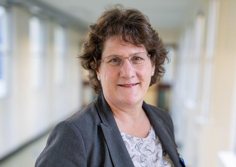 The head of Queen Elizabeth Hospital, Alice Webster, wears a grey jacked and a cream shirt. Her curly brown has is cut short above her shoulders. She is wearing glasses