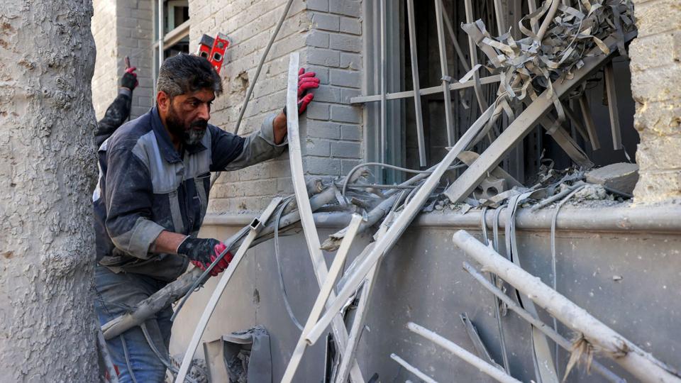 A man inspects damage as bent schrapnel protrude from a window of a university in Tehran that was hit by a US-Israeli missile attack overnight, in Tehran on 7 April