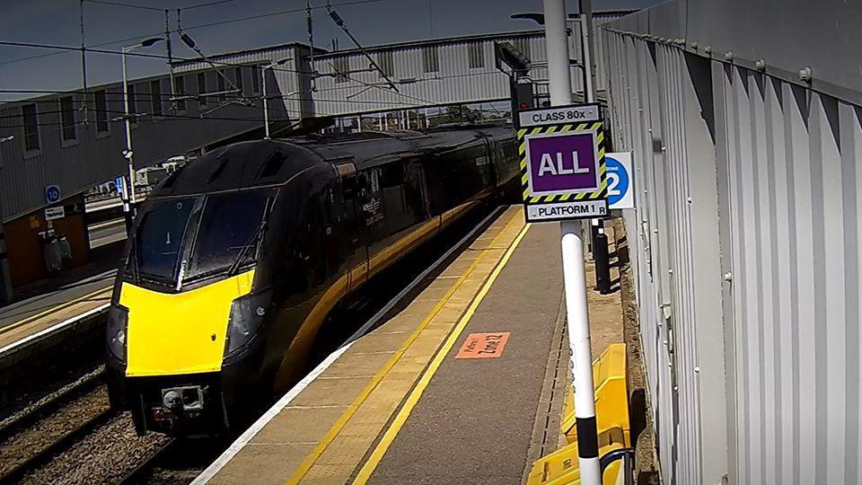 CCTV of a black and yellow train next to a platform