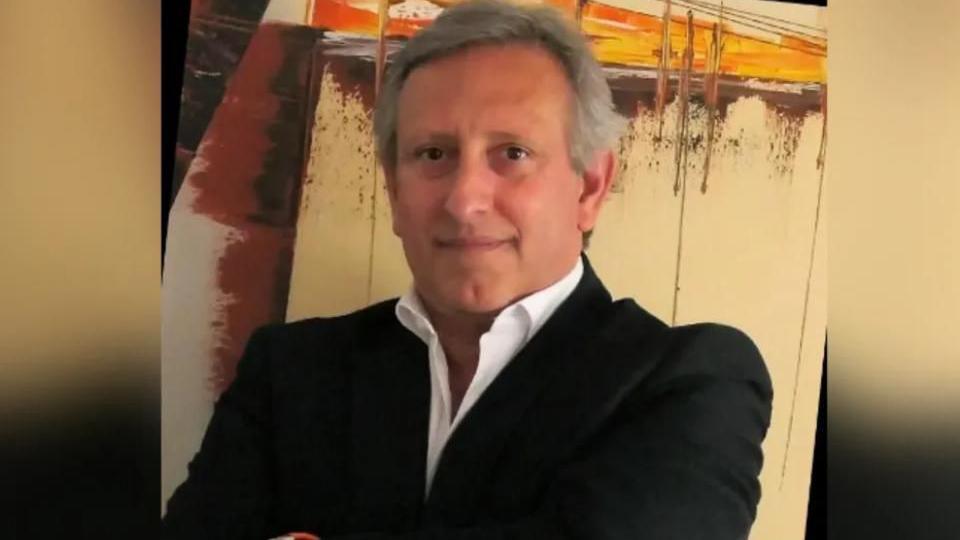 Pedro Trindade, a man with grey hair a black suit and white shirt with no tie, looks at the camera