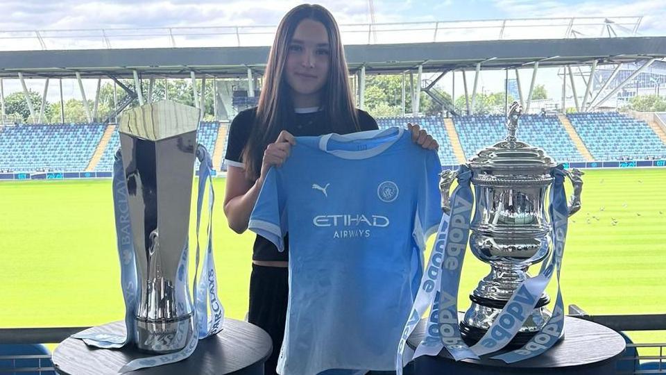Molly Stroud holds up a Manchester City shirt at the academy stadium