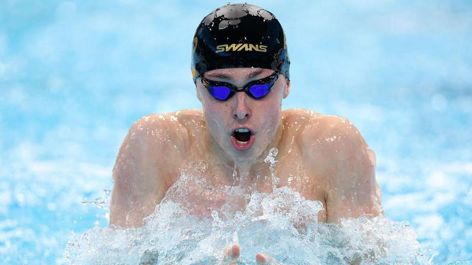 Filip Nowacki mid-stroke during a race. He is wearing a black swim cap and goggles
