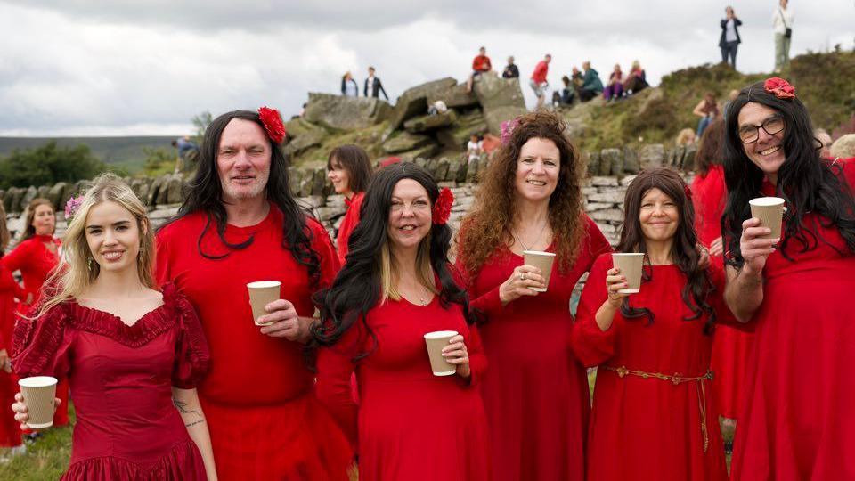 A group of men and women dressed in red holding paper cups while standing in a group on the moors in Yorkshire.