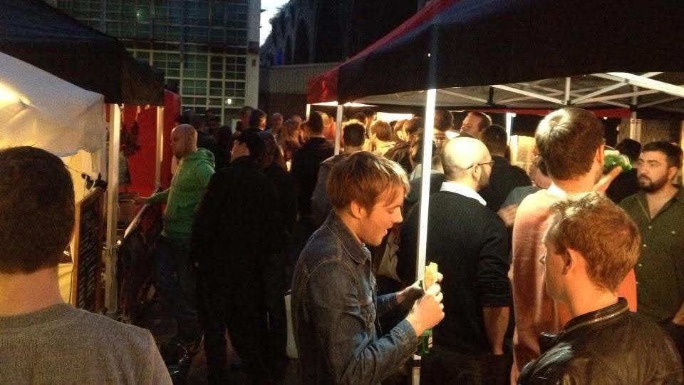 Dozens of people stand under large tents eating street food and talking.