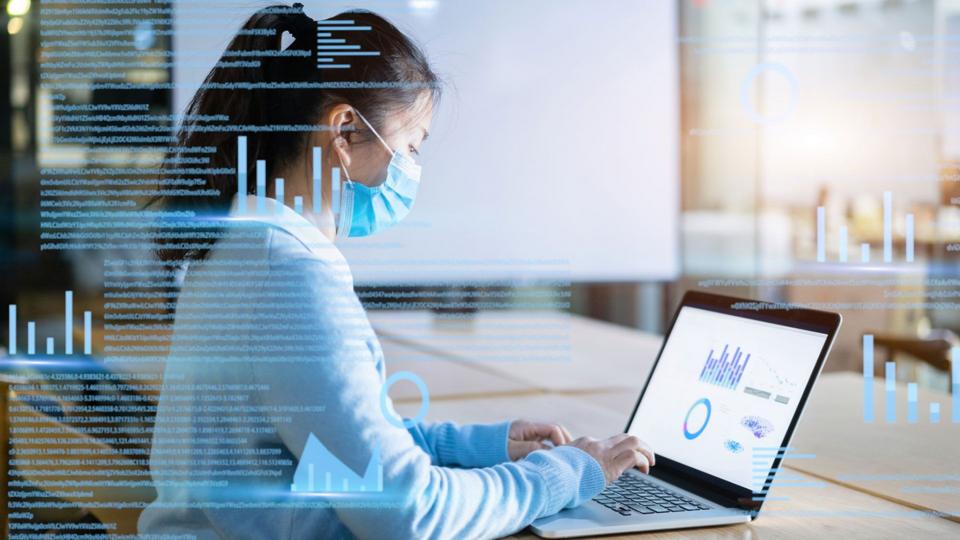 Businesswoman with protective face mask works on virtual visual screen in office.