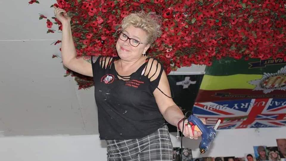 Julie Cooper placing red poppies on the ceiling. She's got blonde curly hair and is holding a glue gun.