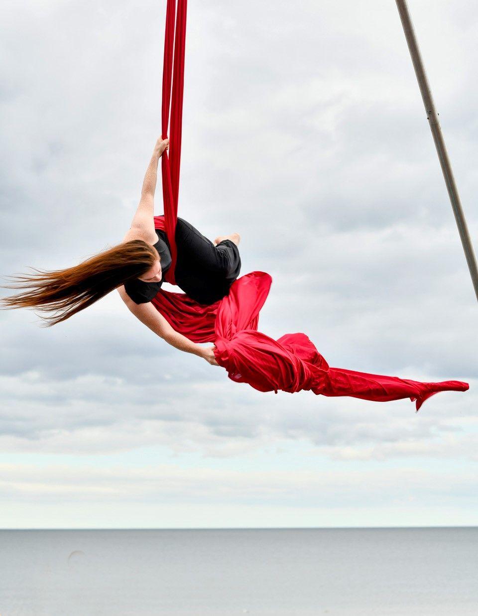 A woman with long hair hangs from a red ribbon while performing an act.