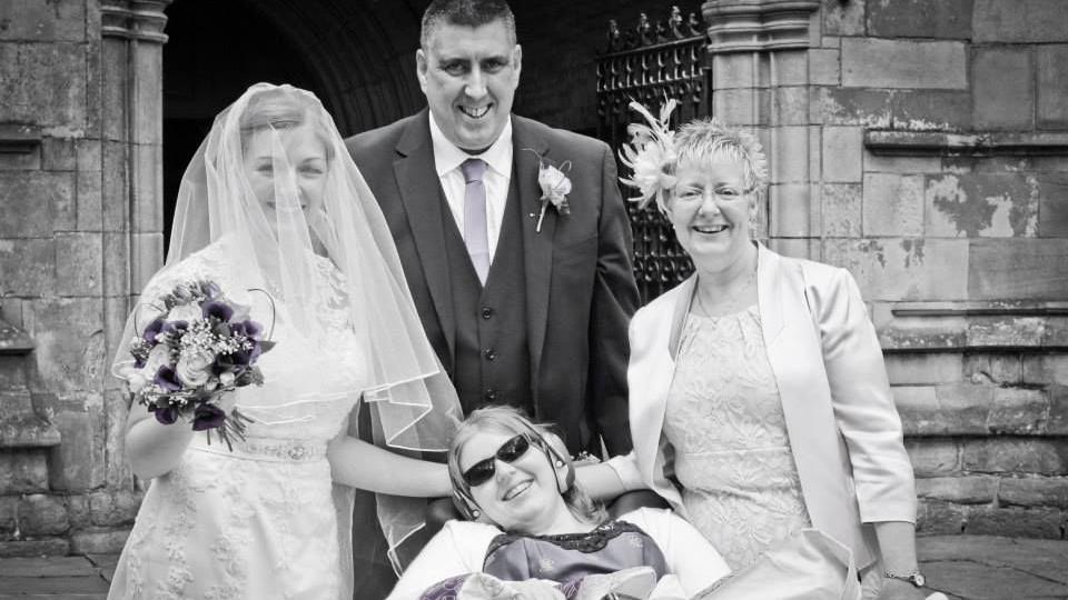 A black and white wedding photo of a smiling bride and her family, who include Kara Jane