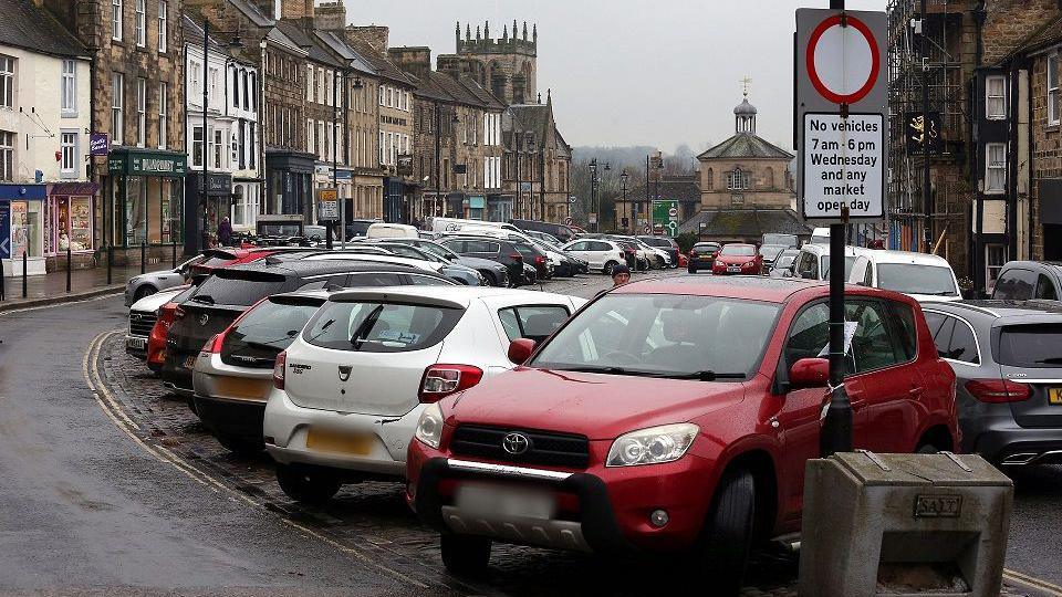 Cars parked on Market Place, looking down towards The Buttermarket in Barnard Castle, County Durham.