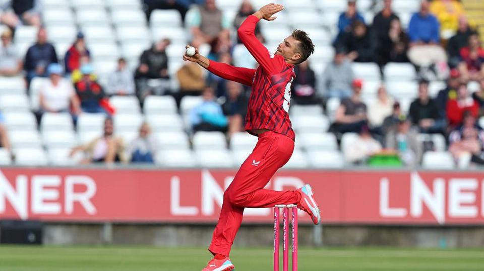 Chris Green, in red kit, in his delivery stride for Lancashire