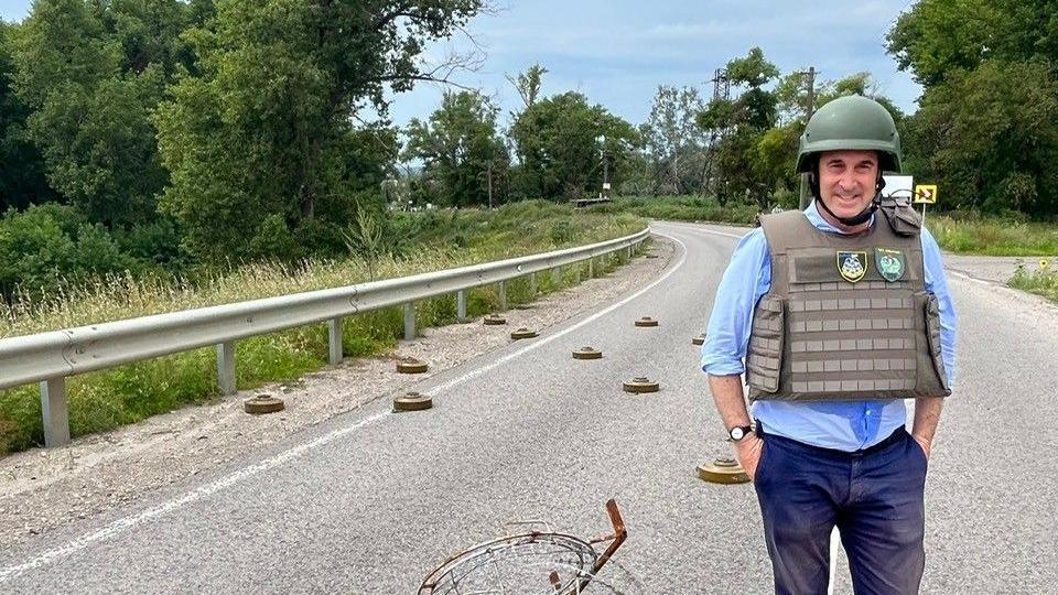 Brooks Newmark wearing protective Army clothing on a road in Ukraine that is dotted with landmines.