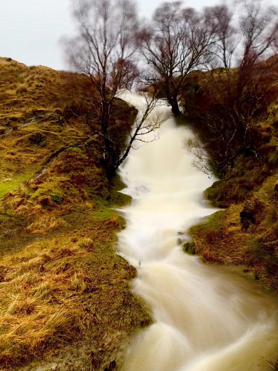 A long-exposure photo of a waterfall running down the centre of the picture surrounded by trees and vegetation