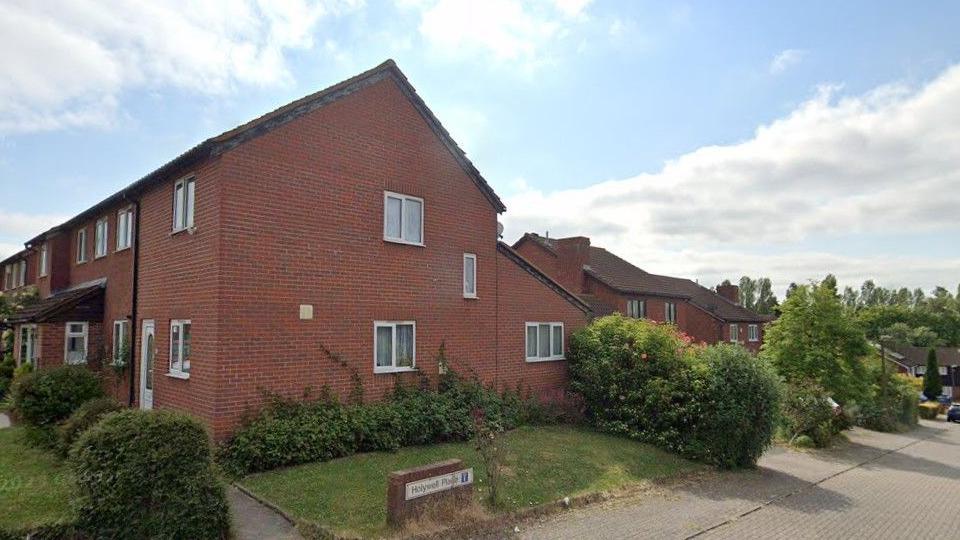 Houses in Holywell Place in Milton Keynes. They are redbrick homes on a small road and there are trees and bushes in the gardens