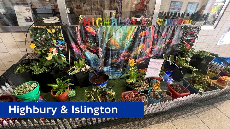 Highbury and Islington is spelt out in a multi-coloured floral arrangement inside a station, surrounded by an array of different coloured potted plants and flowers.