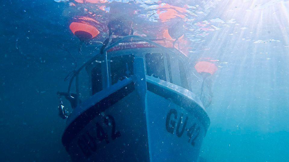 The front of a fishing boat underwater but close to the surface of the ocean.