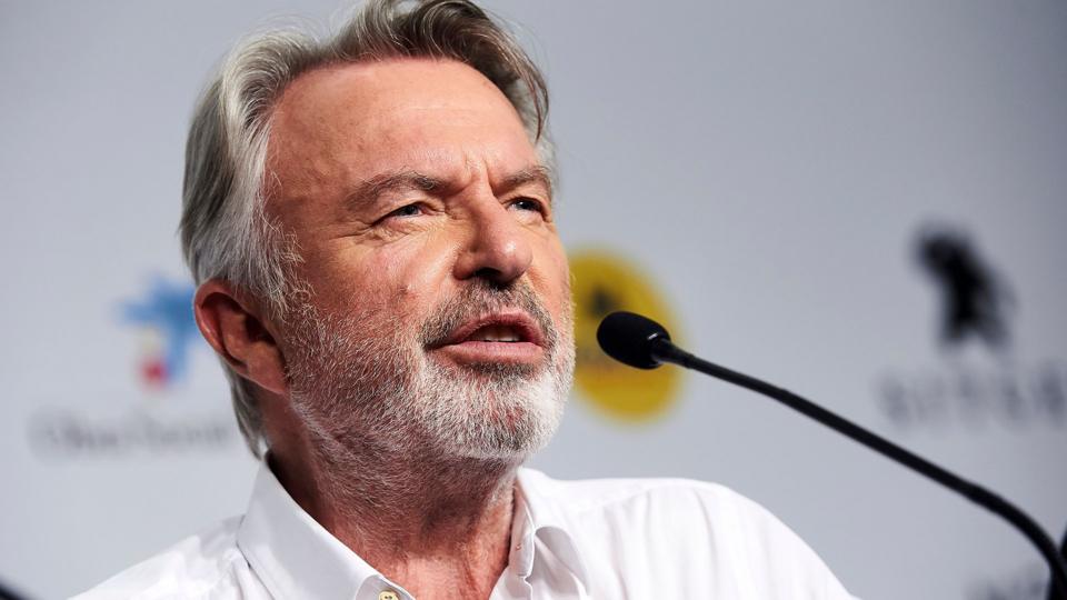 A head and shoulders crop of Neill looking away from camera while speaking into a microphone against a bokeh background, in Spain in 2019.
