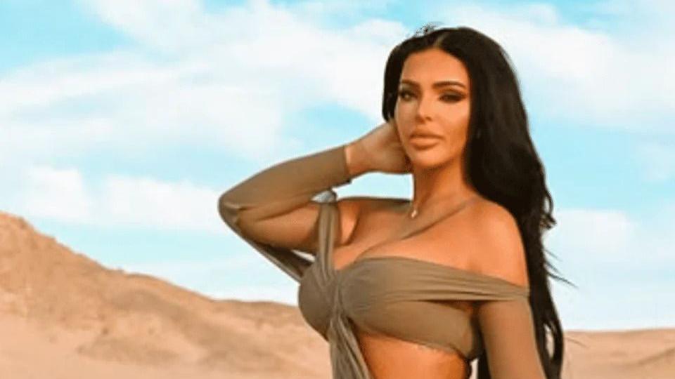Klaudia Zakrzewska in a desert with blue sky. She wears an off-the-shoulder bikini style top which is taupe. Her hair is long and dark and behind her shoulders. She looks directly at the camera and has a small pendant necklace on. 