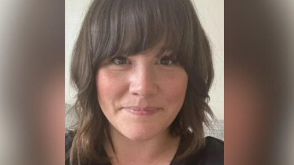 Amy Dewane with shoulder length brown hair, a fringe and smiling at the camera.