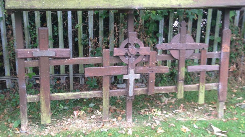 A collection of six wooden crosses of different shapes and sizes, attached to a wooden frame in the cemetery