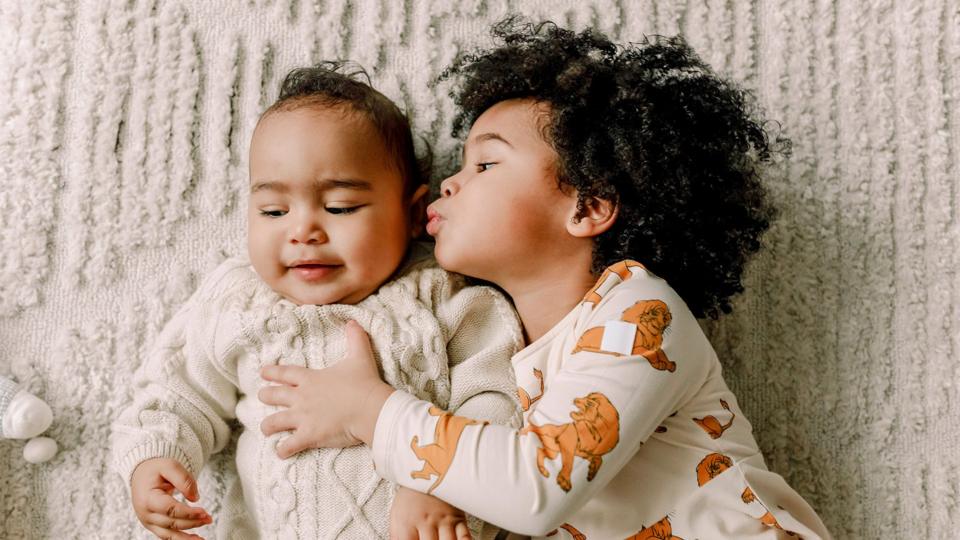 Sister kissing brother lying on blanket at home - stock photo