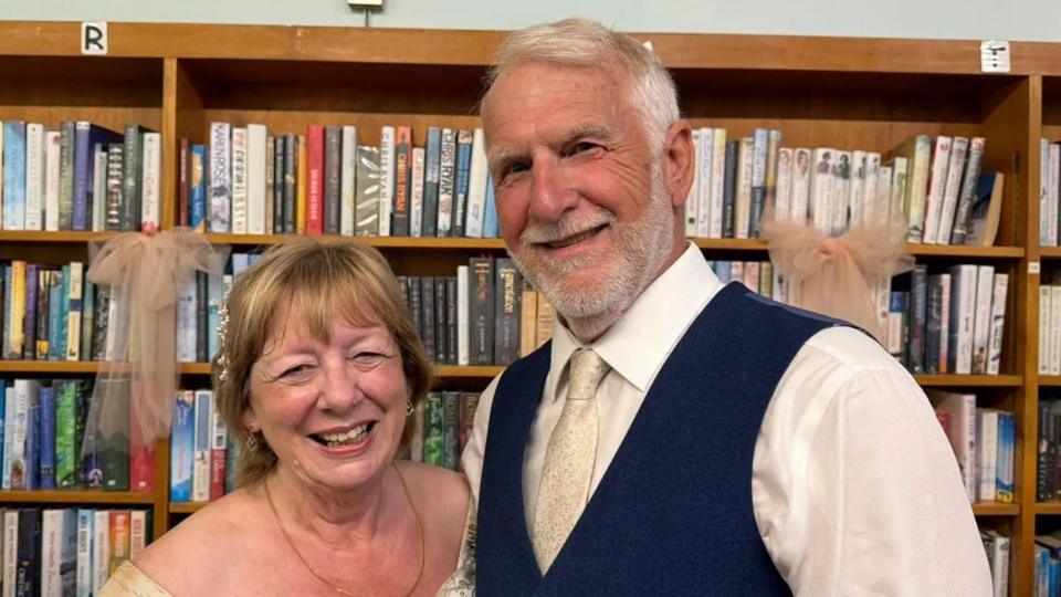 A smiling older couple standing in front of a bookshelf