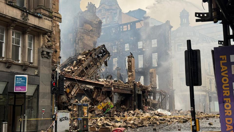 The Union Corner building is reduced to rubble after a fire in Glasgow. Victorian buildings and street furniture surround the iron and sandstone remains.