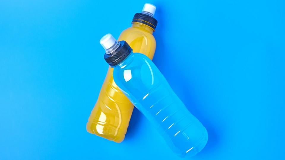 A drinks bottle full of blue liquid, on top of a bottle of orange liquid, on a blue background