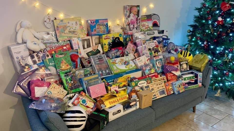 Toys and books arranged on a grey sofa, placed next to a green Christmas tree with colourful balls.