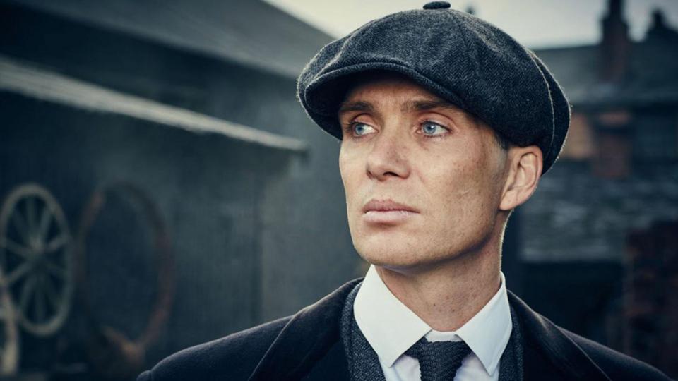 Cillian Murphy as the character of Tommy Shelby in The Peaky Blinders. He is wearing a flat cap, a shirt and tie, and is looking into the distance on the left.