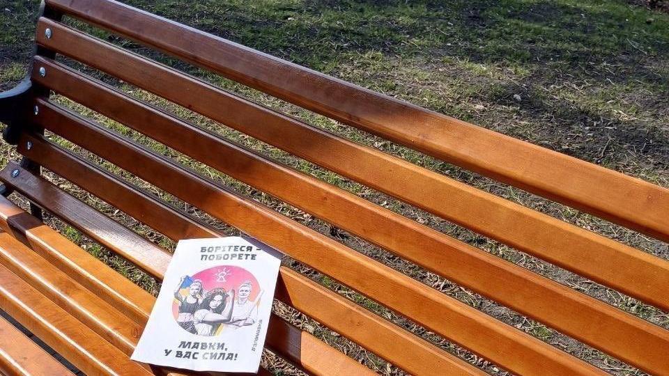 A leaflet on a bench in Melitopol shows a mock-up of three women, one of them holding a Ukrainian flag in blue and yellow
