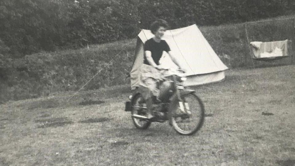 Dorothy Graham in a black and white picture ridig a motorbike with a tent behind