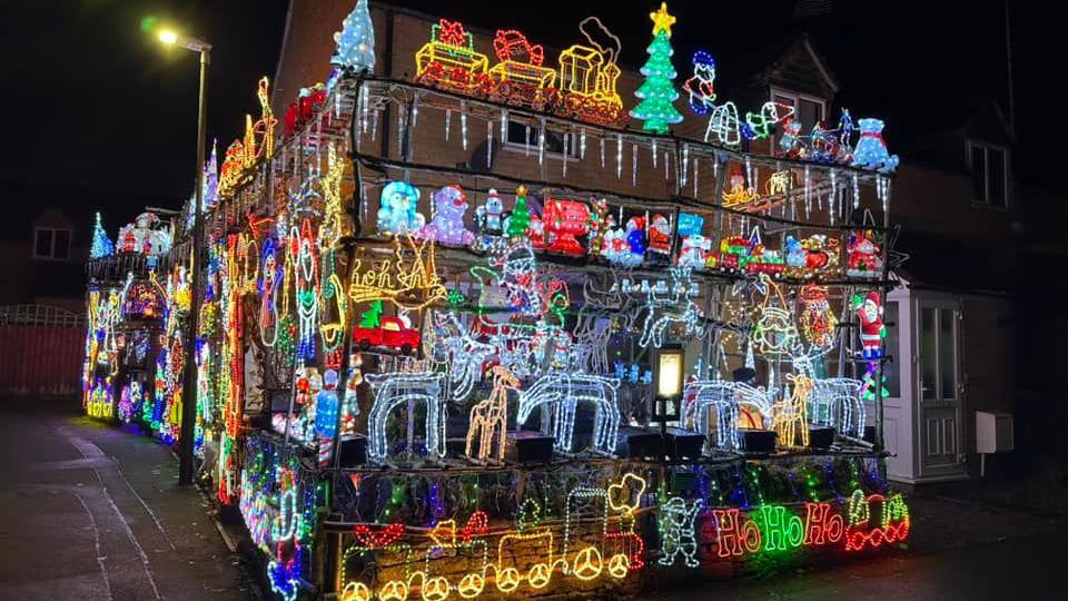 A house in South Cerney, Cirencester. It is covered in multicoloured Christmas lights. Reindeers, Santas, sleighs and trees can be seen. 