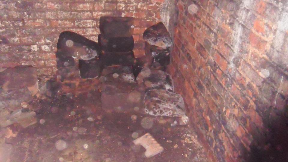 A photograph inside Warstone Lane's catacomb. The image shows a pile of black blocks that appear very mouldy and damp. The inside of the catacomb is made up of red brick. 