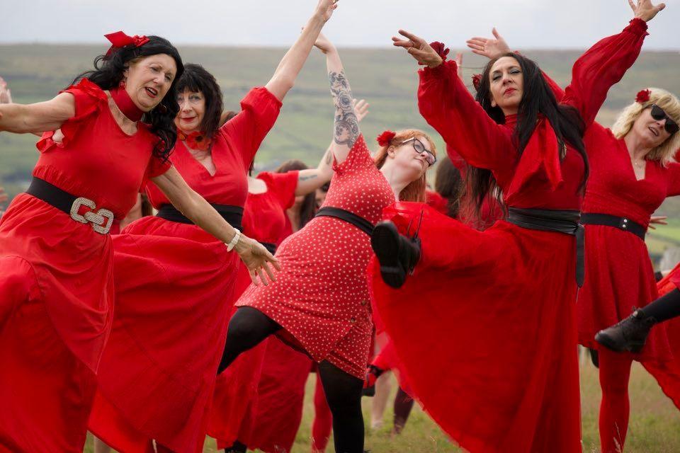 A group of people dressed in red dresses with black belts, dancing on the moors in Haworth 