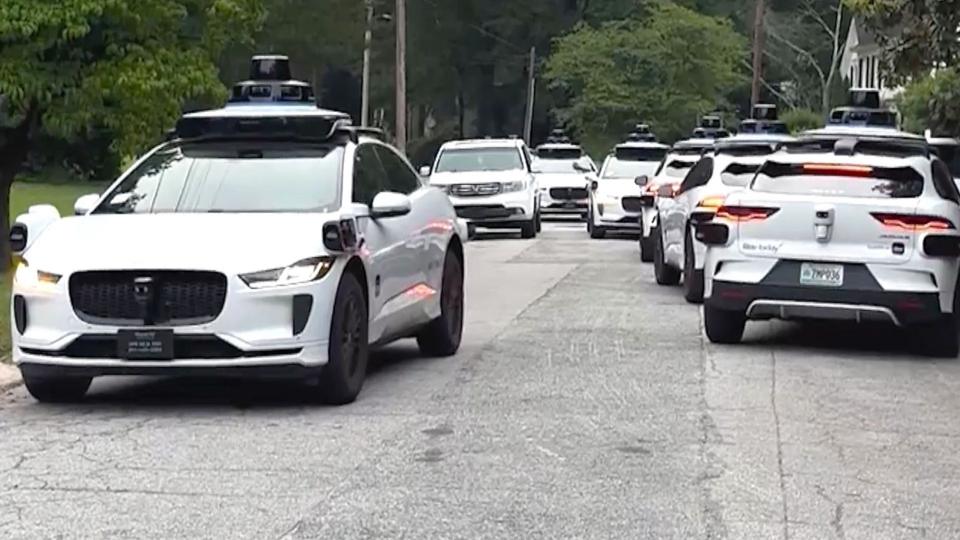 A group of Waymo cars take up all the space in a street.