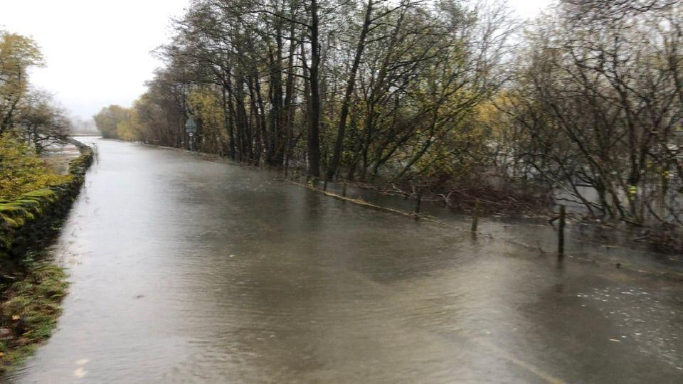 A road which has been flooded by a nearby water source in Borrowdale. The levels are so high it almost reaches the height of a mossy dry stone wall.
