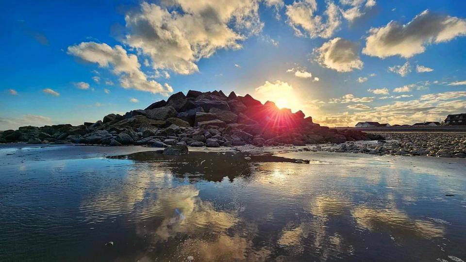 Rocks and sky reflecting into water with the sun in the background