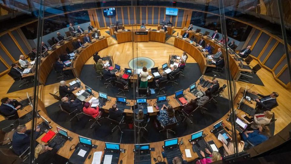 A general view of the Senedd debating chamber full of politicians seen from above. 