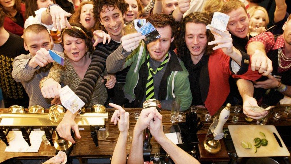 Drinkers in a busy pub try and get bartender's attention