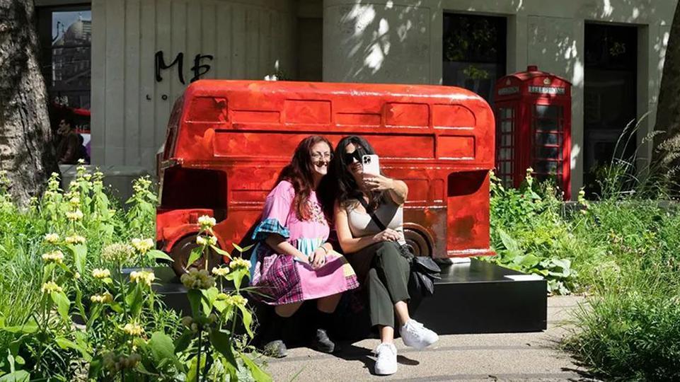 two women taking a selfie infront of london bus sculpture