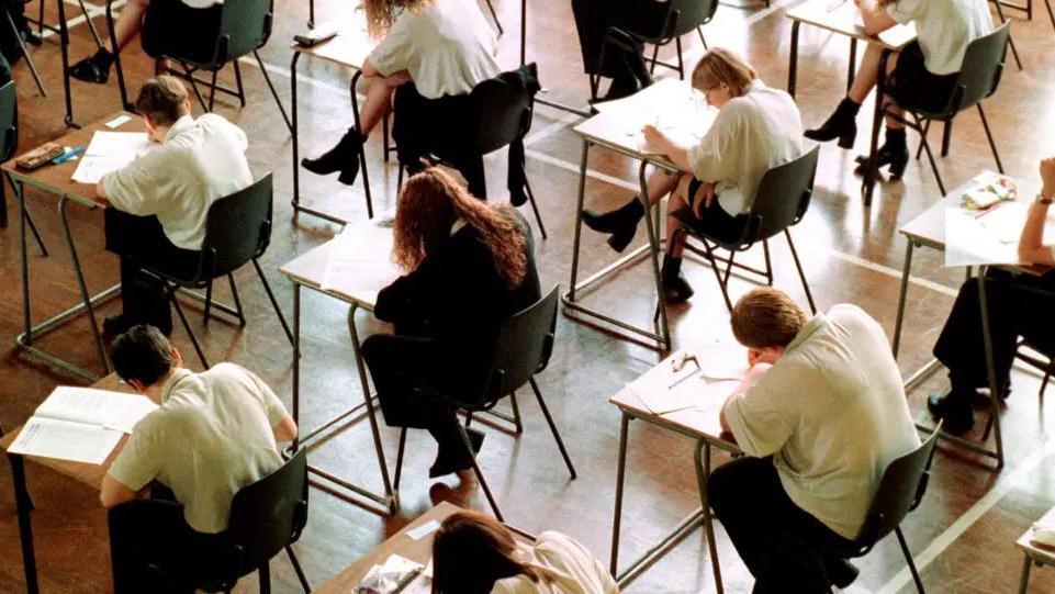 Shot from above of anonymous pupils in an exam hall writing on papers