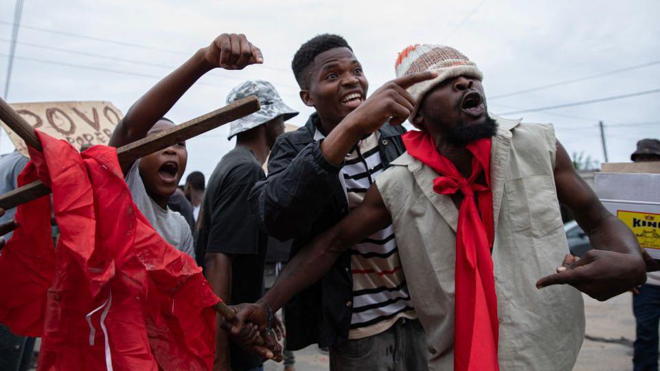 Protesters shouting and pointing in Maputo. A hand-made sign can be seen in the background - Thursday 31 October 2024