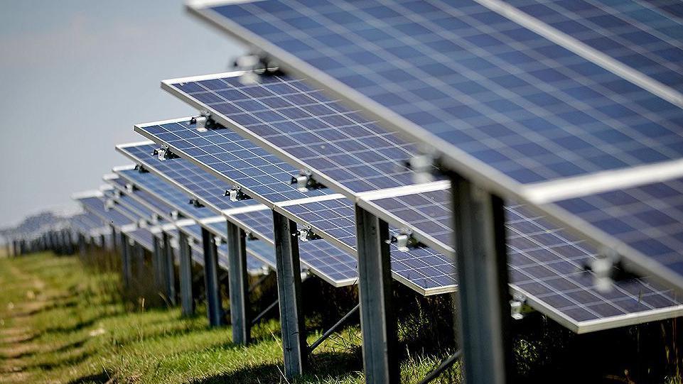 A field with a row of solar panels to the left, gradually fading into the distance