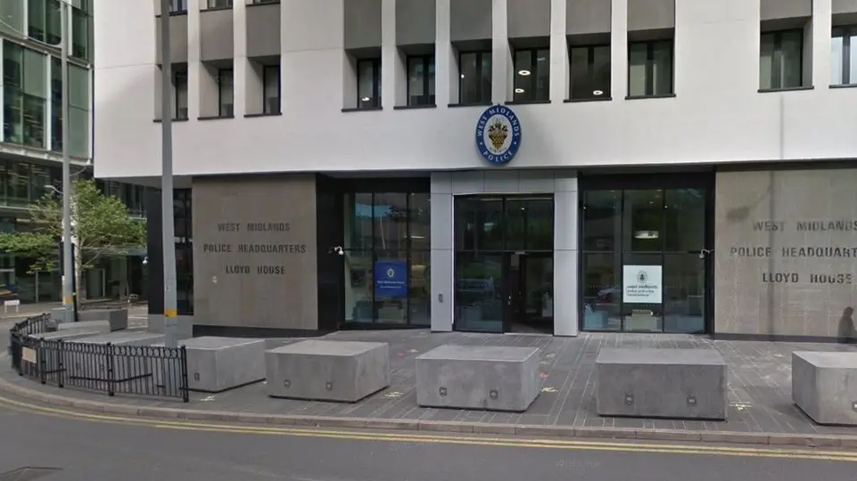 The entrance to West Midlands Police headquarters is pictured. It has concrete blocks outside a stone and glass-fronted building with offices above.
